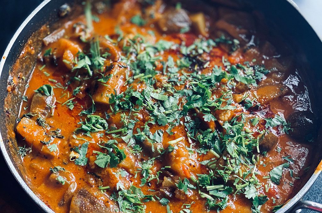 Eggplant curry in a black pot, with coriander spinkled on top